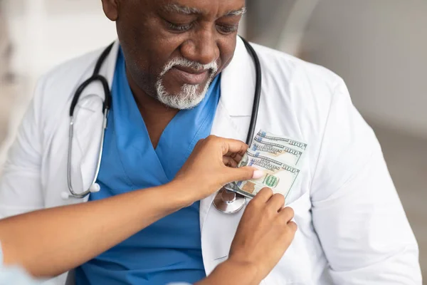 Чорна жіноча рука кладе гроші в кишеню лікарів — стокове фото