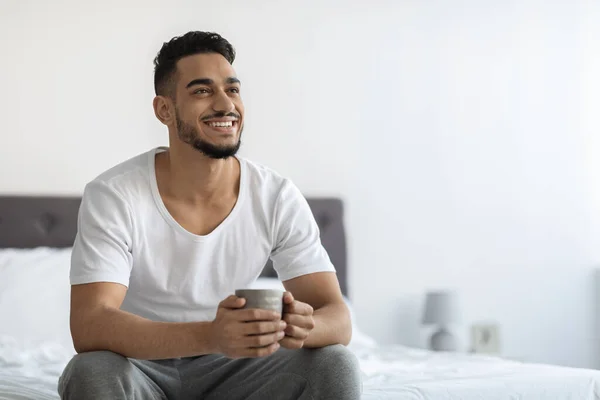 Feliz joven árabe relajándose en la cama con una taza de café — Foto de Stock