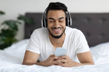 Modern Teknolojiler. Yakışıklı Orta Doğulu Çocuk Akıllı Telefonla Yatakta Rahatlıyor