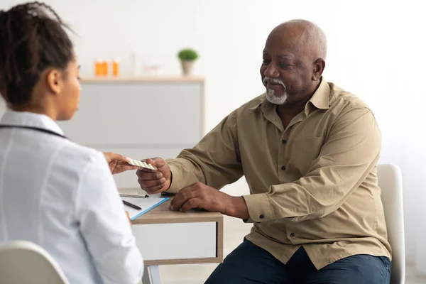 Женщина-чёрный врач показывает таблетки пациенту-мужчине — стоковое фото