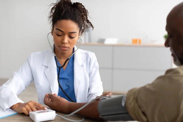Zwarte vrouwelijke arts controleren van de meetdruk op patiënten hand — Stockfoto