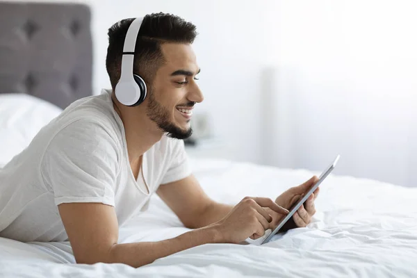 Joven árabe alegre que relaja con la tableta digital en la cama — Foto de Stock