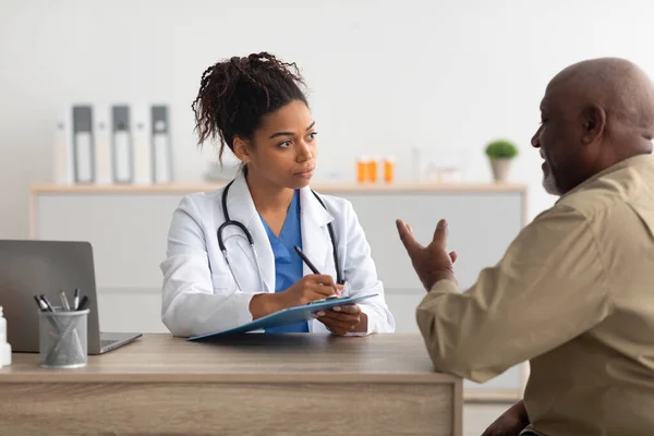 Joven médico negro explicando plan de tratamiento al paciente masculino —  Fotos de Stock