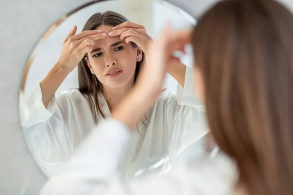 Problema Pele. Perturbação jovem fêmea Popping Pimple na testa perto do espelho — Fotografia de Stock