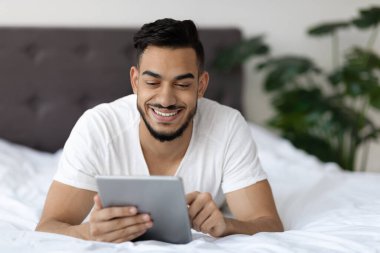 Yatakta dinlenirken dijital tablette interneti tarayan yakışıklı bir Arap.