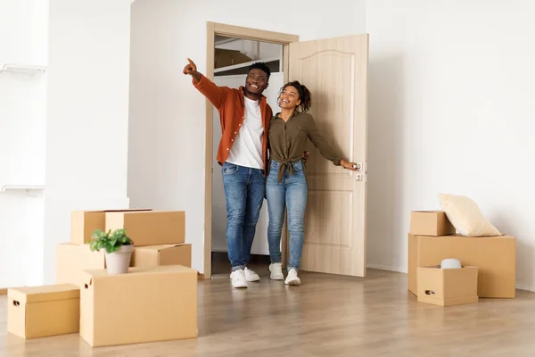Izgatott fekete házastársak belépnek az új otthonukba, a férj a másik oldalra mutat — Stock Fotó