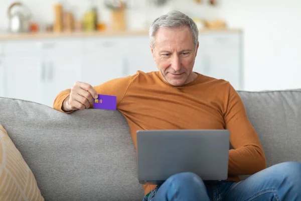 Casual ώριμος άνθρωπος χρησιμοποιώντας το PC και την πιστωτική κάρτα στο σπίτι — Φωτογραφία Αρχείου