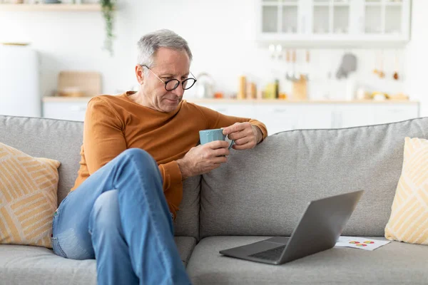 Hombre maduro viendo vídeo en la computadora, beber café —  Fotos de Stock