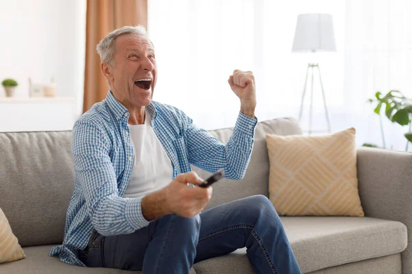 Izgatott érett férfi tévénézés ünneplő cél gazdaság távirányító — Stock Fotó