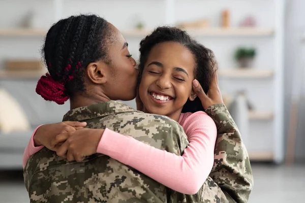 Loving black mother in military uniform kissing daughter
