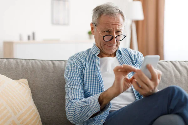 Mature man squinting using mobile phone, looking at screen — Stock Photo, Image