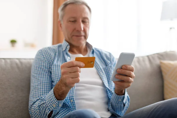 Ώριμος άντρας που χρησιμοποιεί τηλέφωνο και πιστωτική κάρτα στο σπίτι — Φωτογραφία Αρχείου