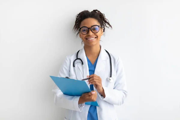 Portrait of black doctor posing with clipboard at white studio — Stock Photo, Image