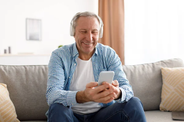 Ευτυχισμένος ώριμος άντρας που χρησιμοποιεί κινητό φορώντας ακουστικά — Φωτογραφία Αρχείου