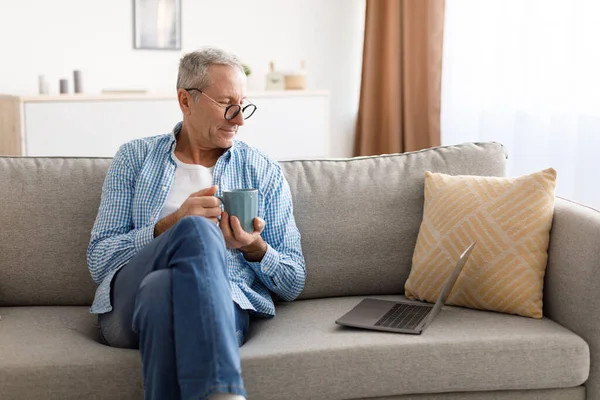 Χαμογελώντας ώριμος άνθρωπος βλέποντας βίντεο στον υπολογιστή, πίνοντας καφέ — Φωτογραφία Αρχείου