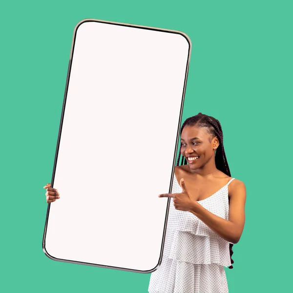 Mulher negra bonita apontando para o smartphone grande com tela branca na mão — Fotografia de Stock