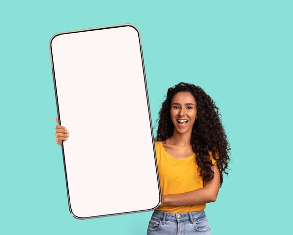 Schöne Millennial-Frau demonstriert großes Smartphone mit weißem Bildschirm vor der Kamera — Stockfoto