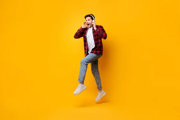 Pemuda bersemangat di headset melompat di studio oranye — Stok Foto