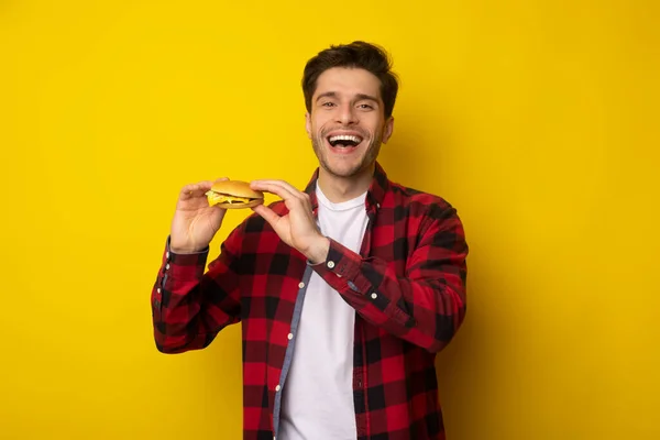 Divertido joven sosteniendo hamburguesa en el estudio — Foto de Stock