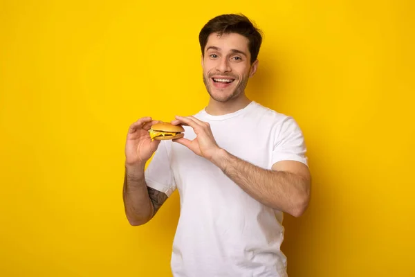 Sorrindo jovem cara segurando hambúrguer no estúdio — Fotografia de Stock