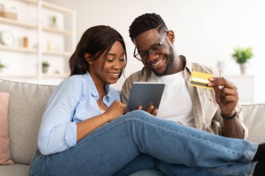 Siyah çift evde tablet ve kredi kartı kullanıyor.