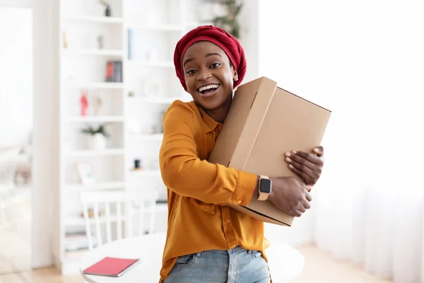 Ekstatische junge schwarze Frau umarmt Box zu Hause — Stockfoto