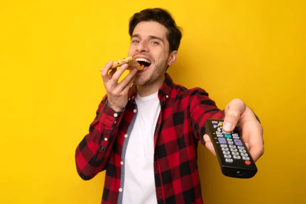 Cara engraçado comendo pizza e segurando controle remoto assistindo TV — Fotografia de Stock