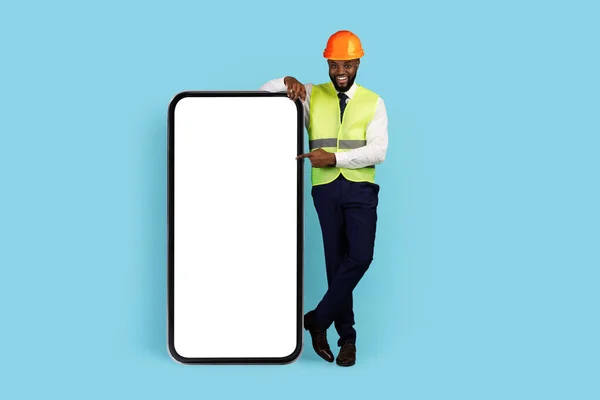 Vše pro stavebnictví. Happy Black Engineer ukazující na velký prázdný Smartphone obrazovku — Stock fotografie