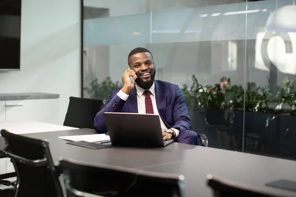 Administrador negro positivo trabajando en la computadora, teniendo conversación telefónica —  Fotos de Stock