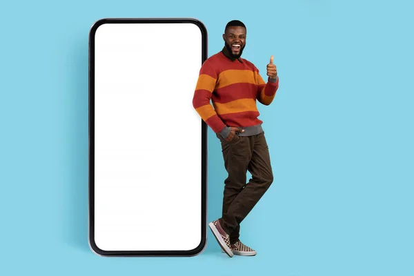 大きな空白のスマートフォンの近くに立って親指を表示楽しい黒人男性 — ストック写真