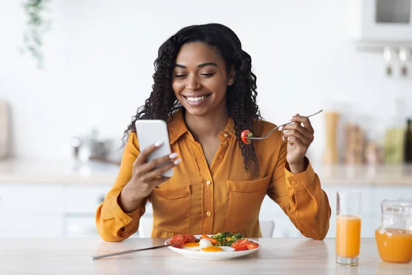 Felice donna nera che naviga sui social media mentre fa colazione — Foto Stock