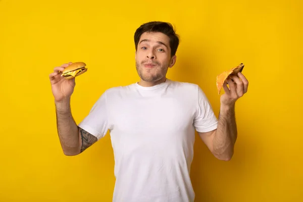 Chico divertido sosteniendo hamburguesa y rebanada de pizza —  Fotos de Stock