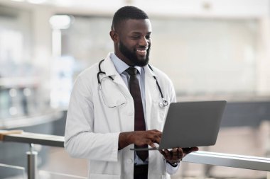 Gülümseyen Afro-Amerikan doktor elinde dizüstü bilgisayar, klinik içi