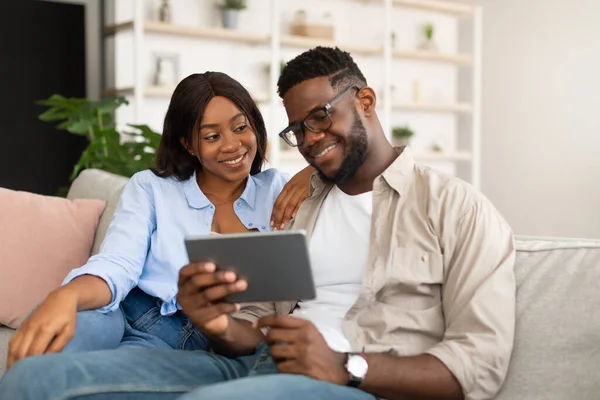 Preciosa pareja afroamericana sentada en el sofá, usando la tableta —  Fotos de Stock