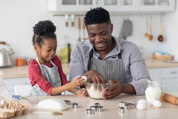 Gadis hitam kecil menambahkan telur sementara ayahnya membuat adonan — Stok Foto