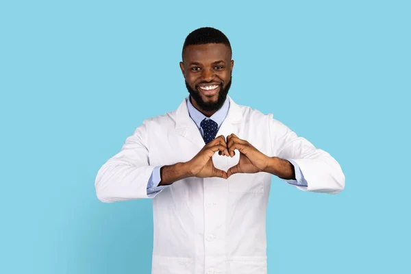 Lächelnder afroamerikanischer Arzt in Uniform macht Herzzeichen mit den Händen — Stockfoto