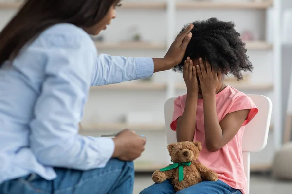 Afroamerikanerin tröstet emotionales lockiges Mädchen im Vorschulalter, Klinik-Innenraum — Stockfoto