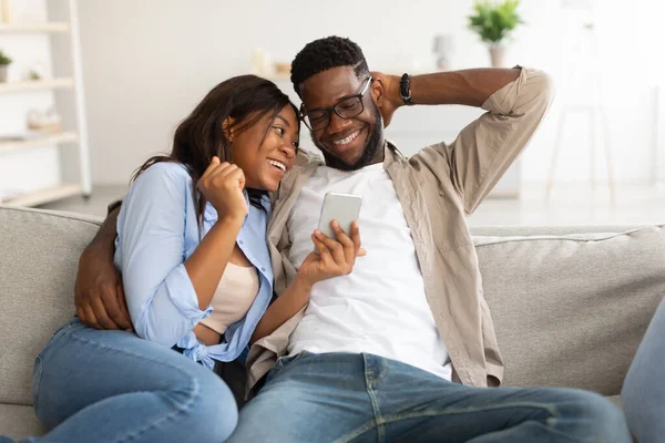 Afrikanisch-amerikanisches Paar sitzt auf Couch und benutzt Handy — Stockfoto