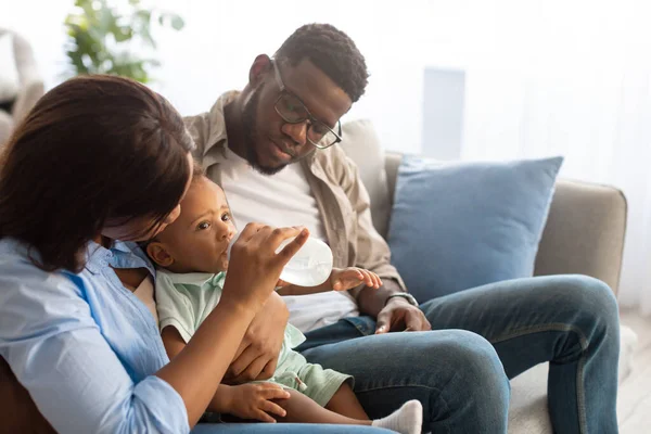 Молодые афроамериканские родители кормят ребенка из бутылки — стоковое фото
