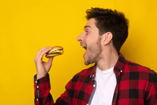 Divertido tipo hambriento sosteniendo hamburguesa mordiendo sándwich en el estudio —  Fotos de Stock