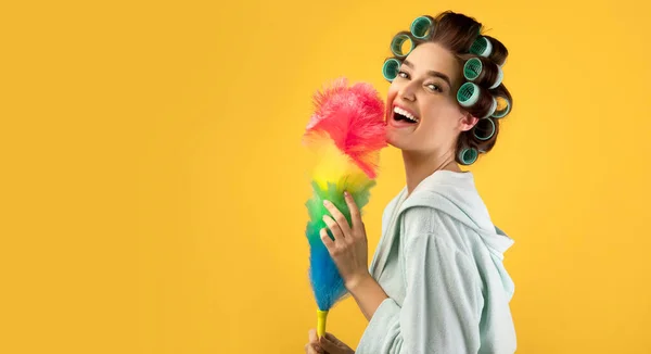 Mulher feliz com encrespadores de cabelo segurando espanador de penas, fundo amarelo — Fotografia de Stock