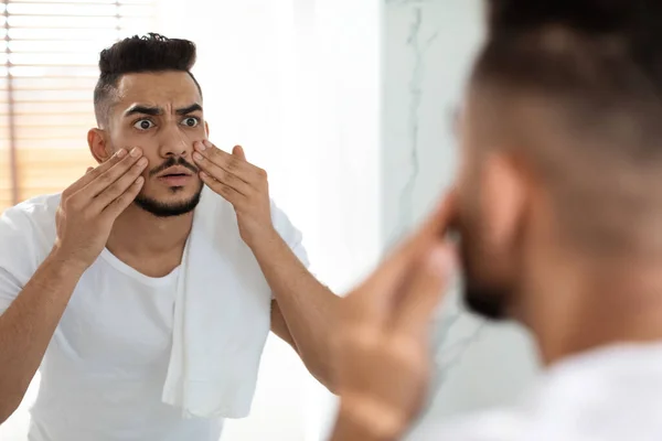 Dull Skin Concept. preocupado árabe chico mirando en espejo y conmovedor cara — Foto de Stock