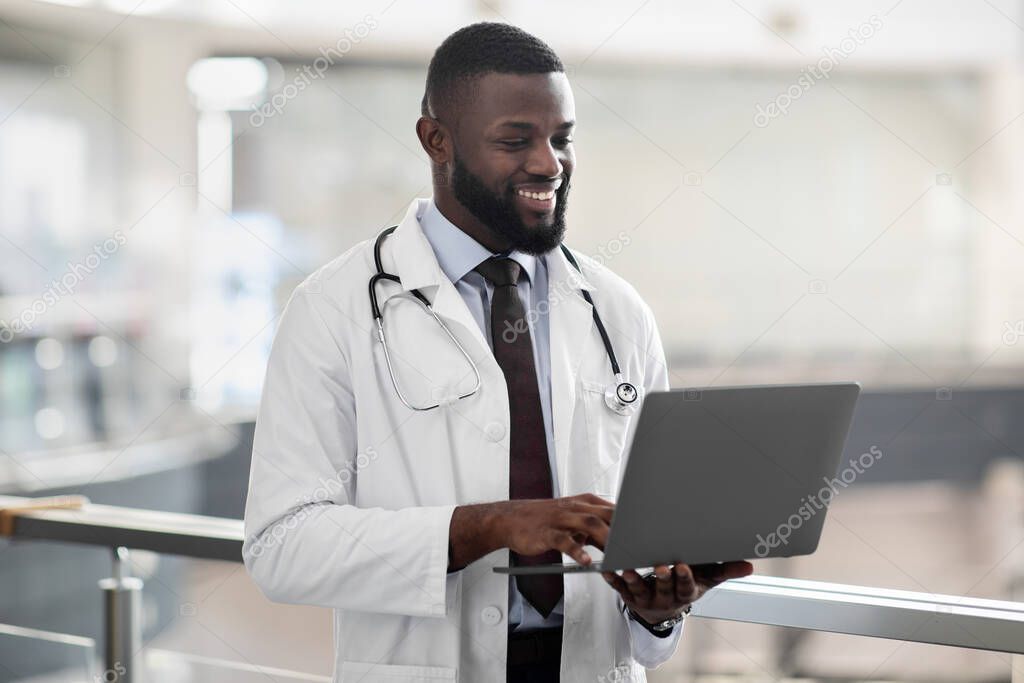 Smiling african american doctor holding laptop, clinic interior