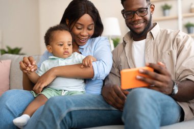 Evde bebekle cep telefonu kullanan Afrikalı Amerikalı bir aile.