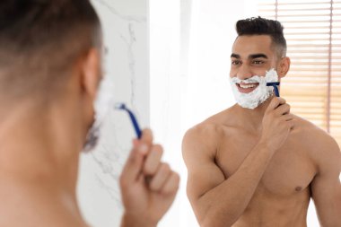 Yakışıklı Gömleksiz Arap Adam Banyoda aynaya bakarken yüzünü tıraş ediyor