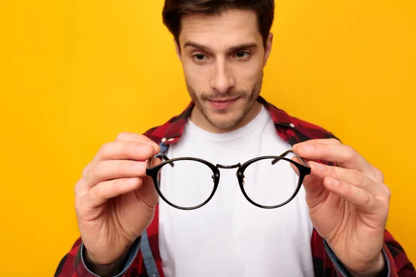 Nahaufnahme eines jungen Mannes, der eine Brille hält und auf sie blickt — Stockfoto