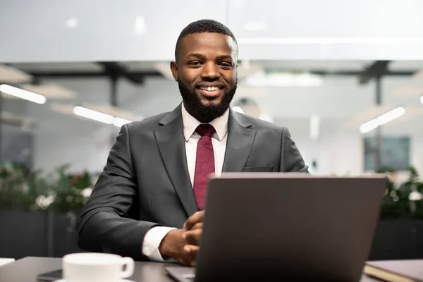 Bonito homem de negócios preto posando na mesa de trabalho no escritório — Fotografia de Stock