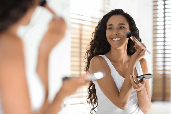Make-up Routine. Fröhliche junge Dame trägt Rouge mit Pinsel in Spiegelnähe auf — Stockfoto