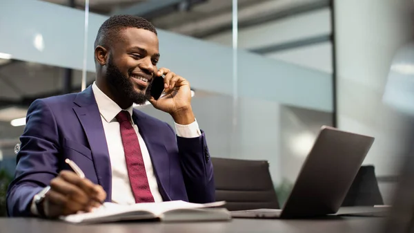 Hombre de negocios afroamericano guapo trabajando en el ordenador portátil, teniendo conversación telefónica — Foto de Stock