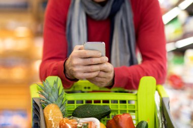 Süpermarkette alışveriş yaparken cep telefonu kullanan bir adam.